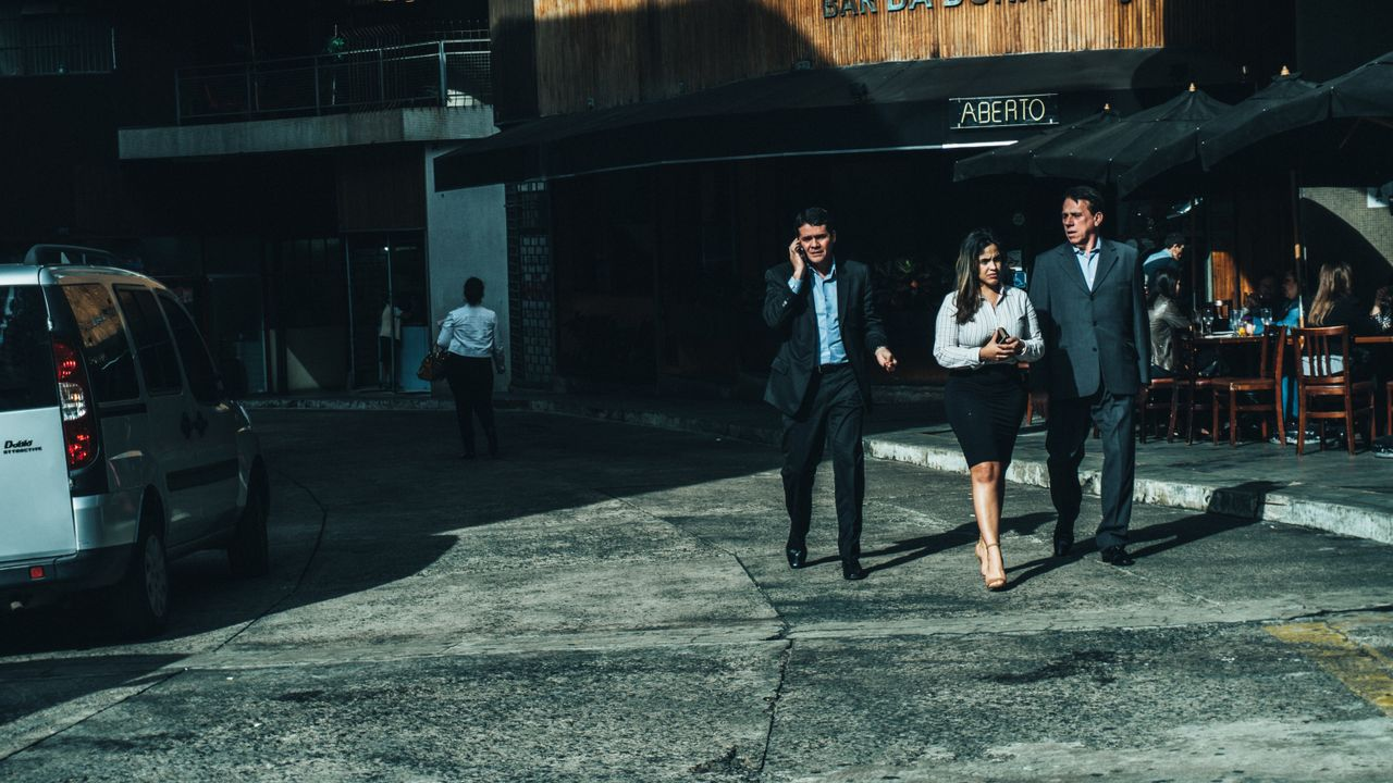 Three business professionals walk along a city street outside a cafe