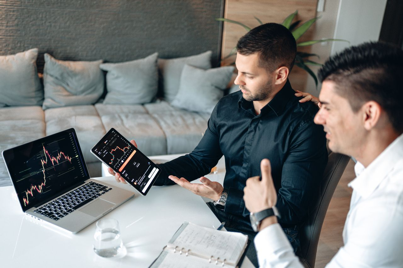 Two people discussing digital trading insights with laptop and tablet
