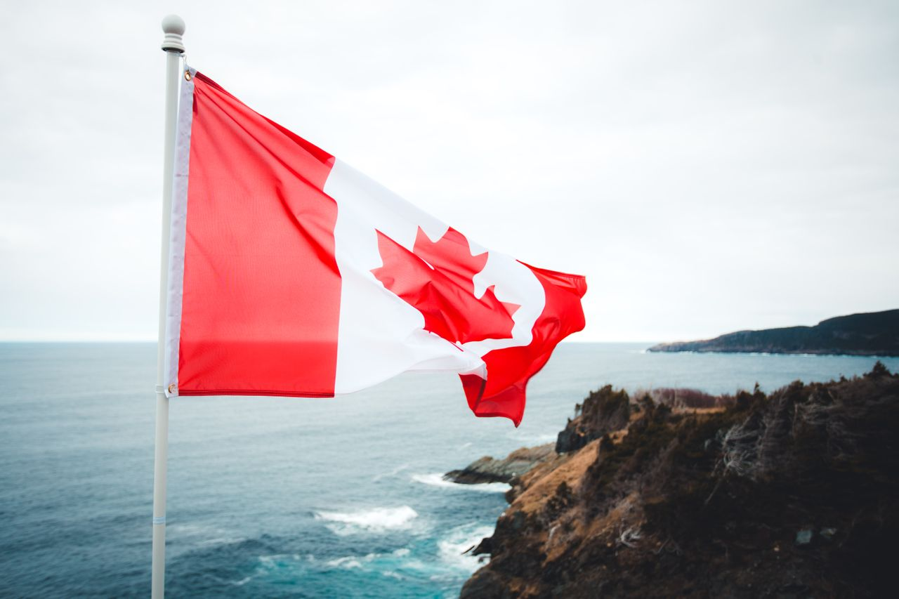 Canadian flag waving over a rugged coastline