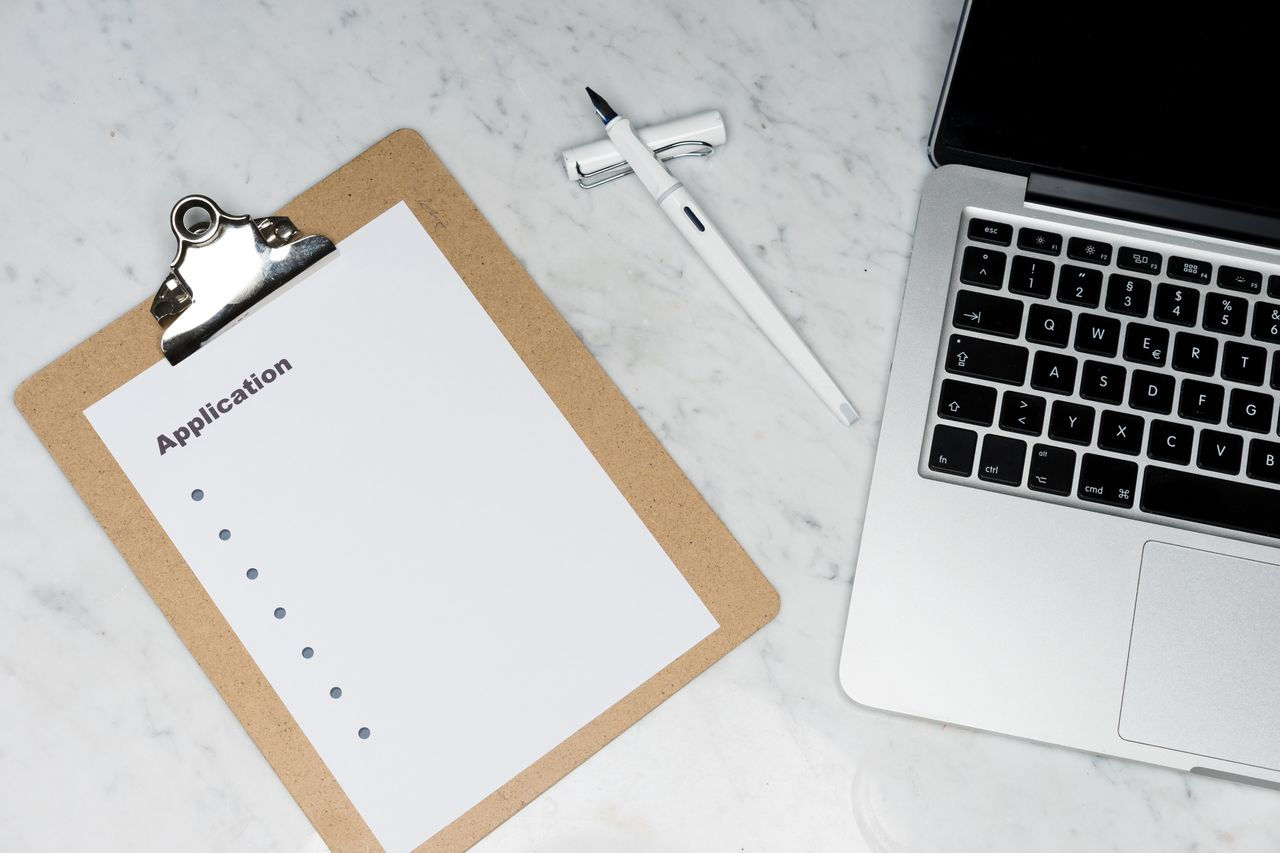 Office desk setup featuring a laptop, clipboard with application form